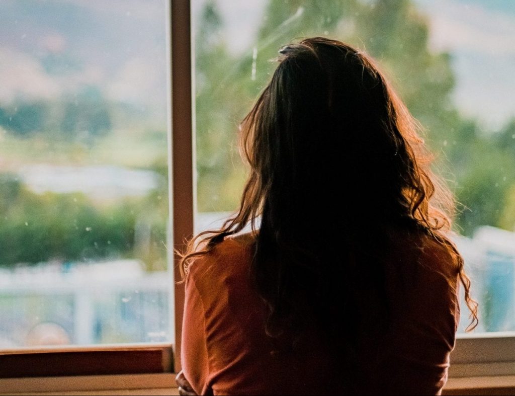 Woman with long brown hair looking out of the window