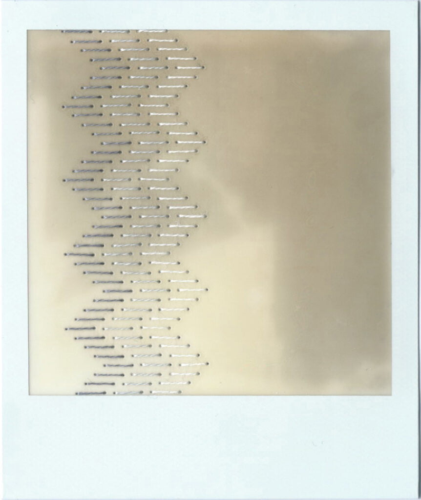 The image is a polaroid, blur of grey and white, a vague imprint of the shadows of some blinds that they sat below on a windowsill. There is a traditional blackwork embroidery pattern stitched down the left hand side of the polaroid. The stitching is done in gradients of grey. On the first photo, the pattern consists of rows of staggered straight lines that give the overall impression of a column of zig zags. 