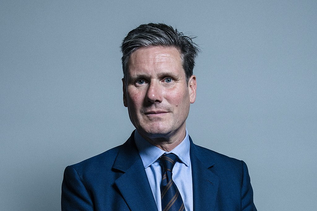 Portrait of Keir Starmer with swept up grey hair, in a blue suit and stripy tie.