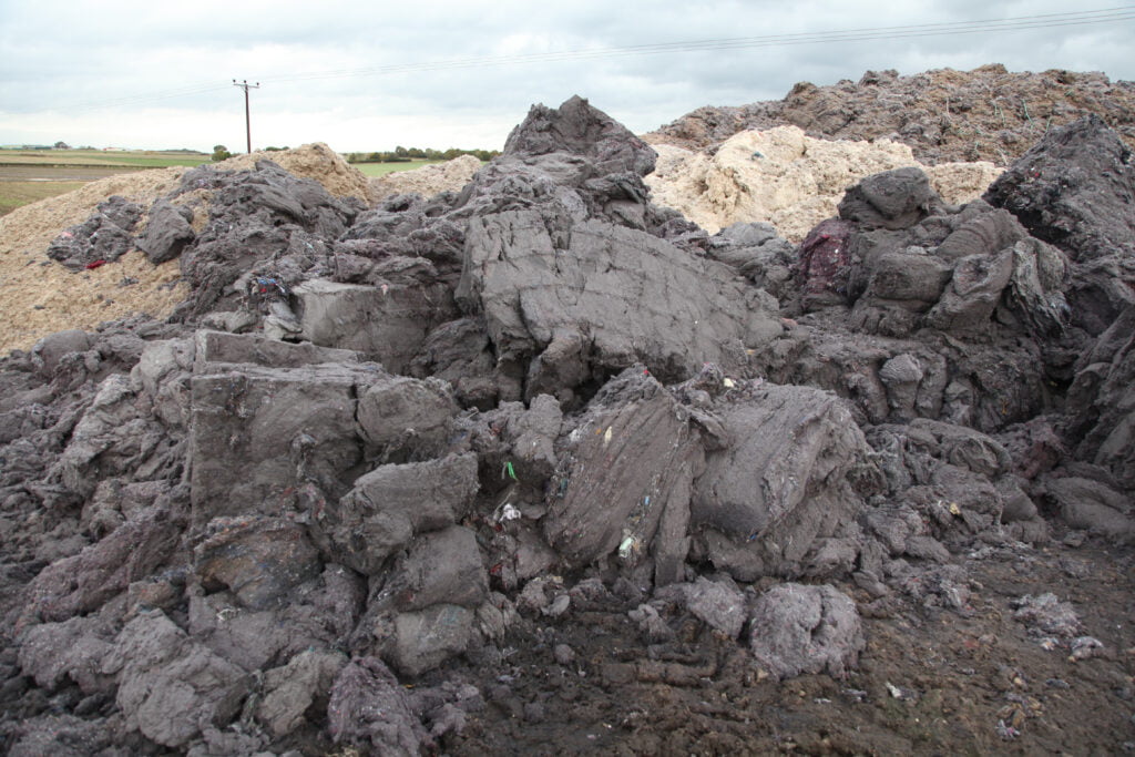 Pile of crumbling shoddy in the field, it looks like very compressed grey fluff.