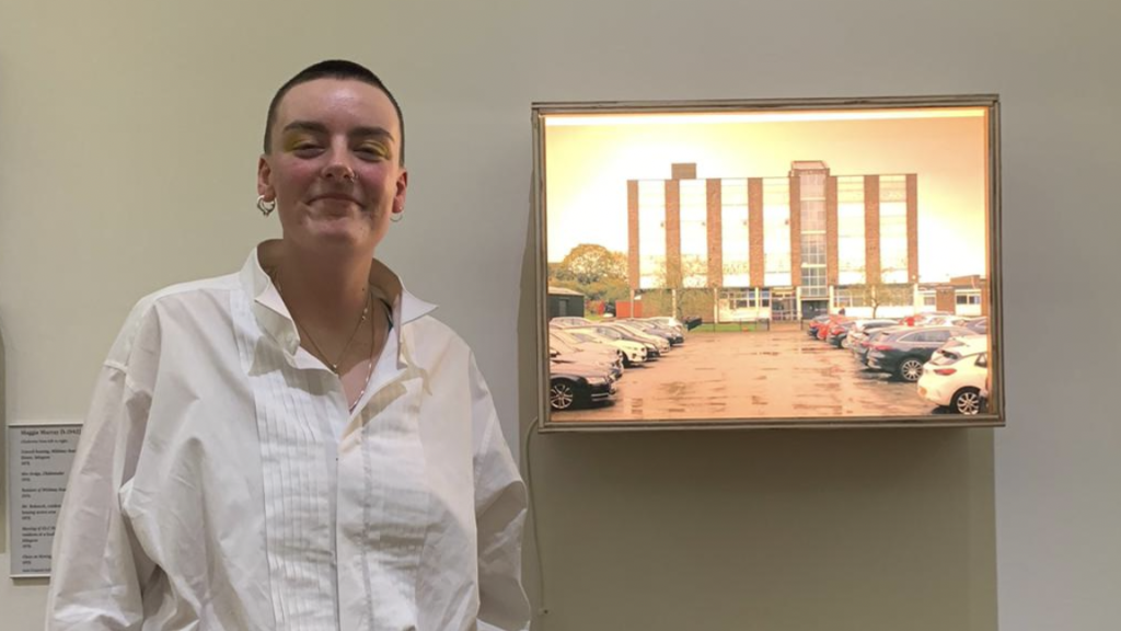 Artist George Storm Fletcher stands in front of a picture of a car park