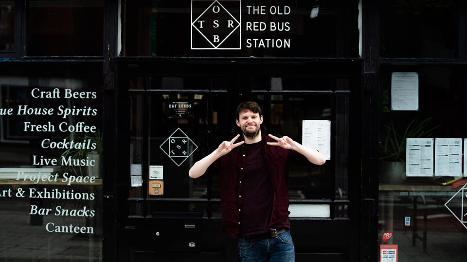 A man in shirt and jeans stands outside a music venue