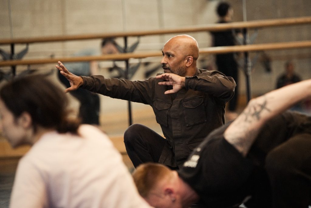 Image of Akram Khan demonstrating dance positions to his dancers. 