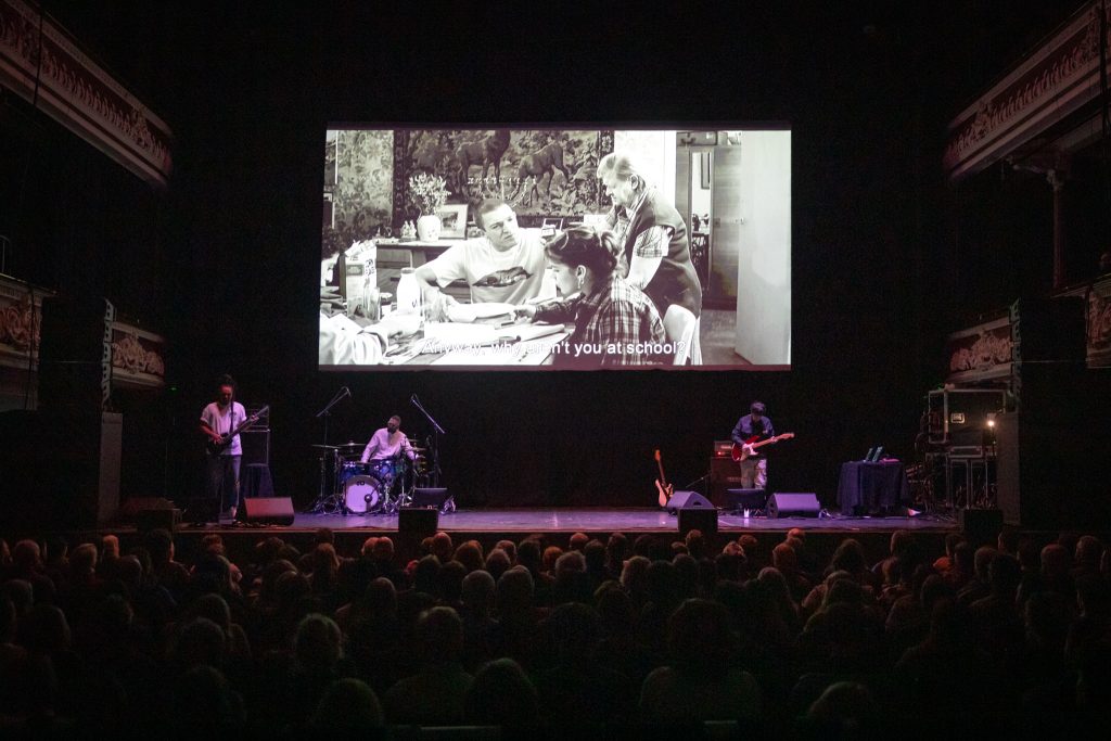 Photo of Asian Dub Foundation, featuring a bass guitarist, drummer and guitarist, on stage in front of an audience