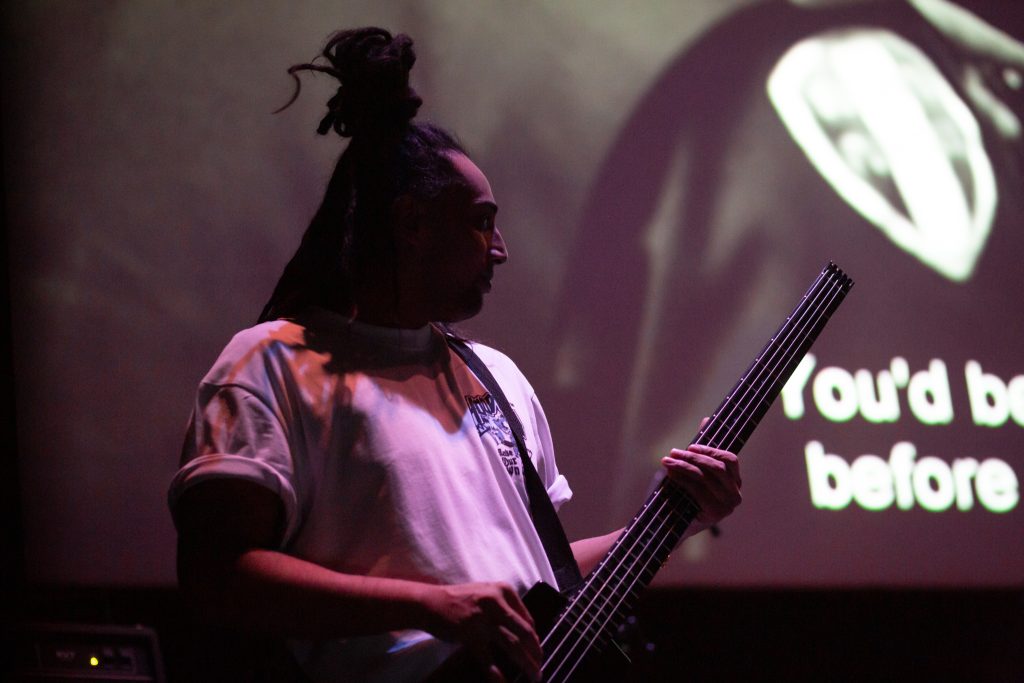 An image of a man in a white top playing bass guitar