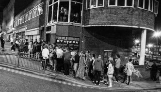 A black and white image of people stood outside a venue