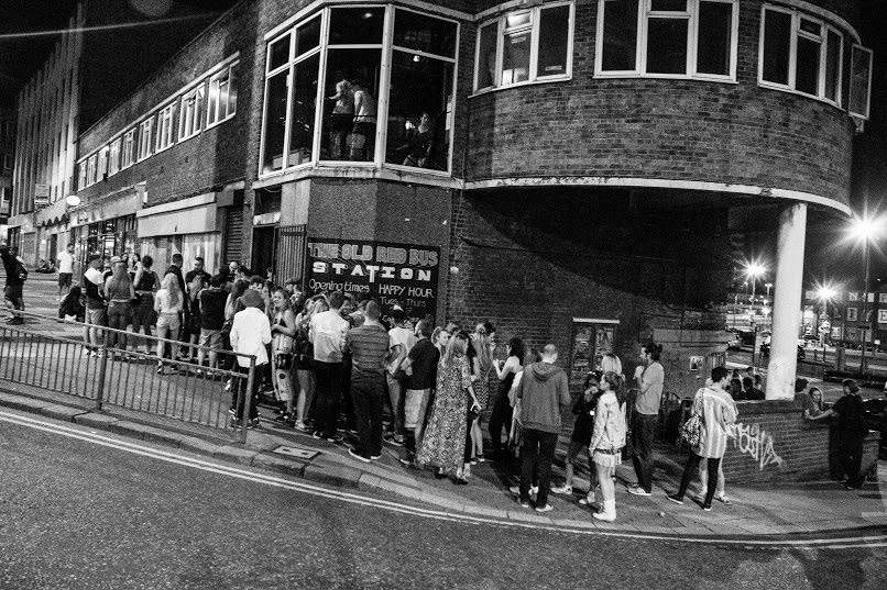 A black and white image of people stood outside a venue