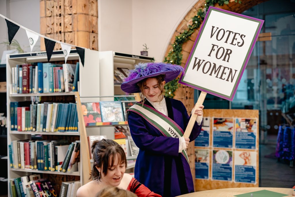 Image of Kate Pankhurst holding a sign saying votes for women. 