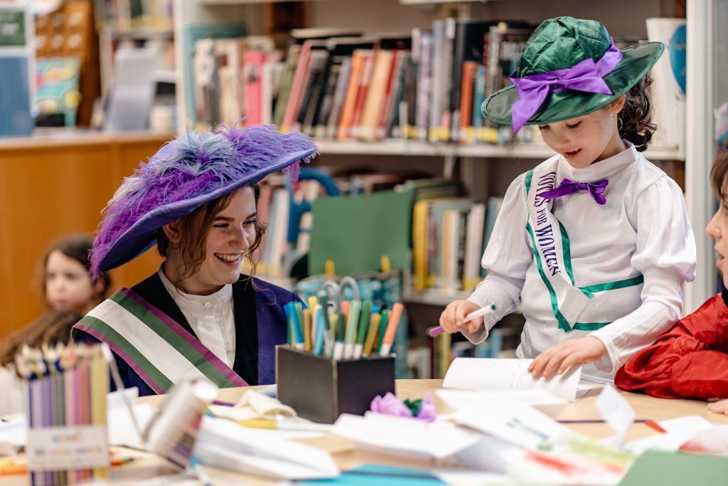 Image of Kate Pankhurst and child dressed up as Emmeline Pankhurst doing crafts. 